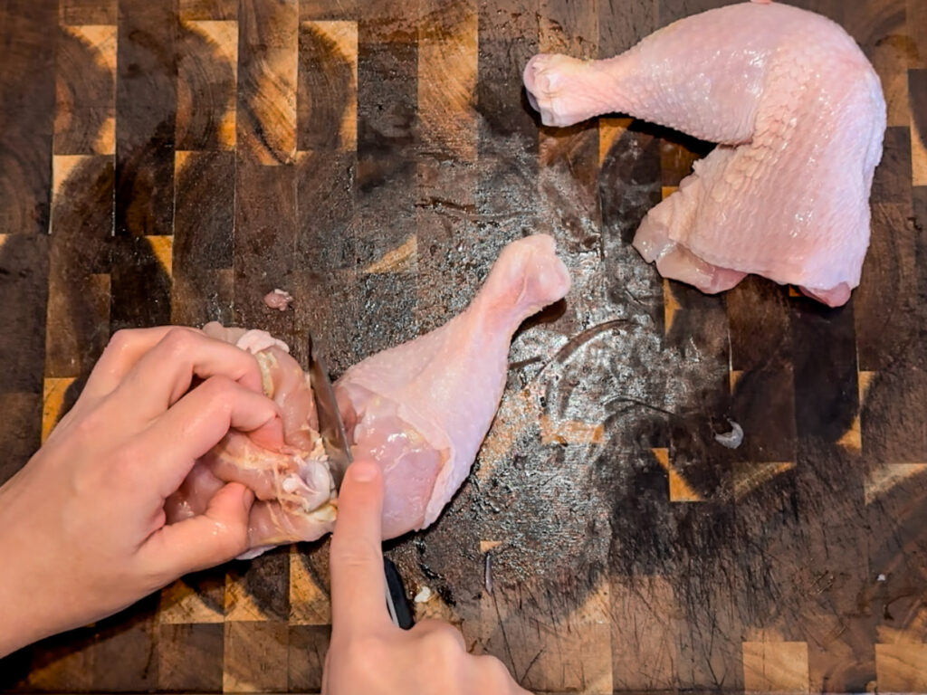 A knife cutting through the joint of a leg and thigh of a chicken. 
