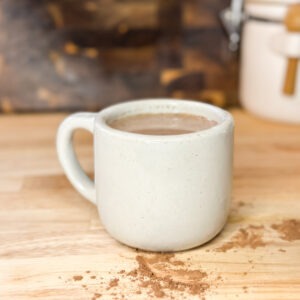 Finished cup of hot chocolate bone broth on a counter dusted with cocoa powder