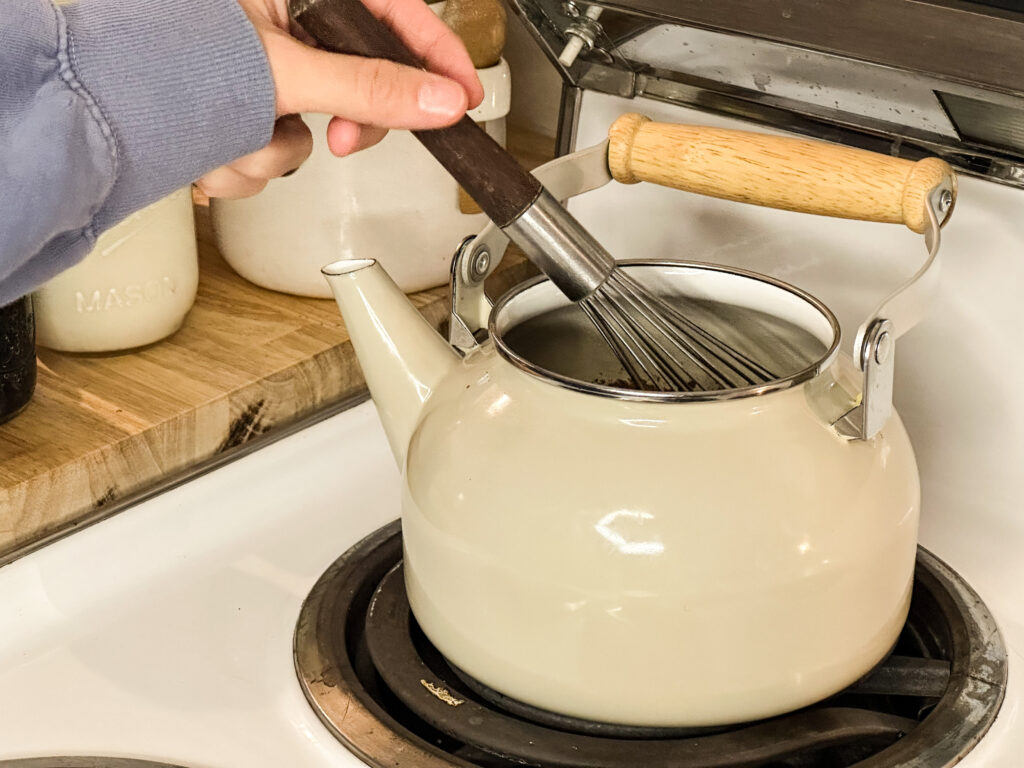 A woman's hand whisking the contents of a tea kettle warming on the stove.