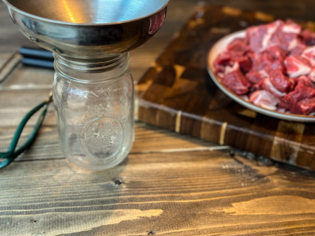 A pint jar with a canning funnel ready to be filled with cubed stew meat for pressure canning