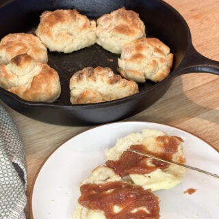 a cast iron skillet of flaky freezer biscuits next to a served biscuit with butter and homemade strawberry rhubarb jam.