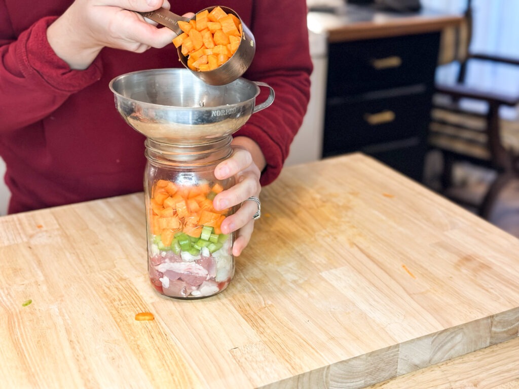 Diced carrots being added to a canning jar of raw turkey and vegetables through a canning funnel.