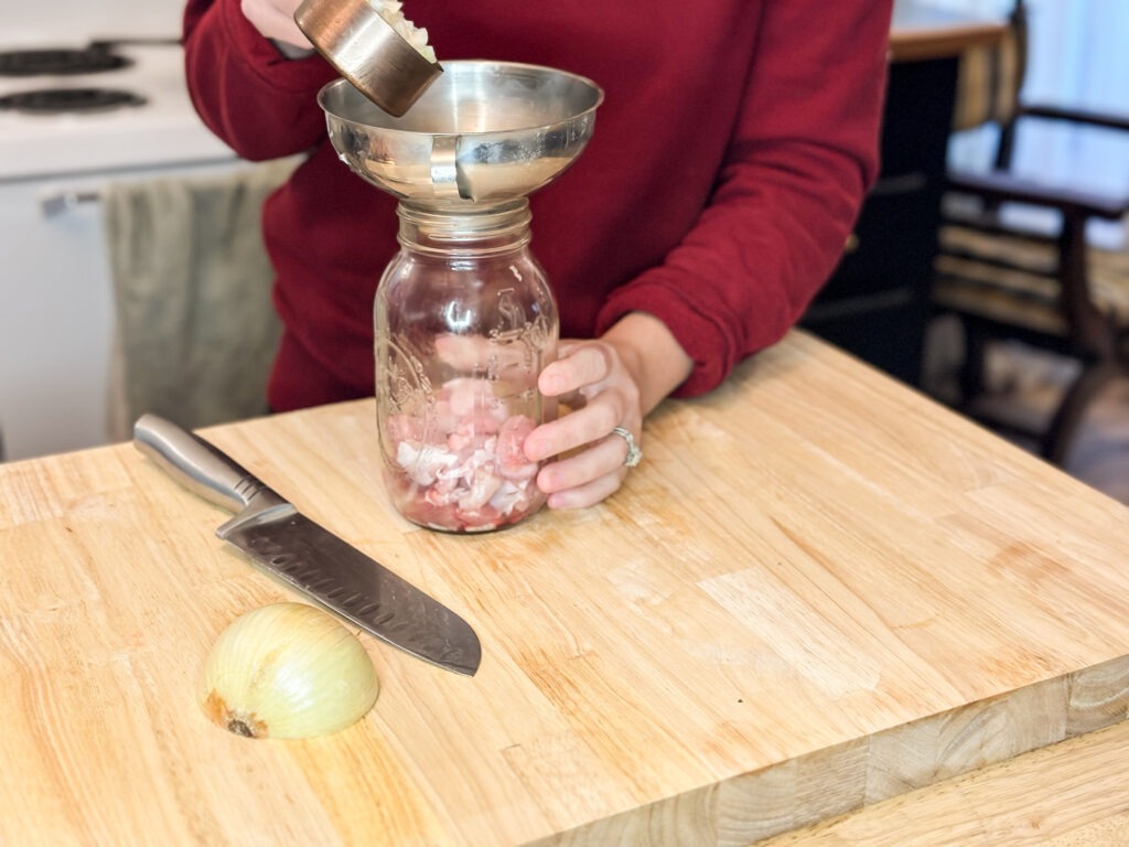 Raw turkey in a quart size mason jar being topped with diced onion