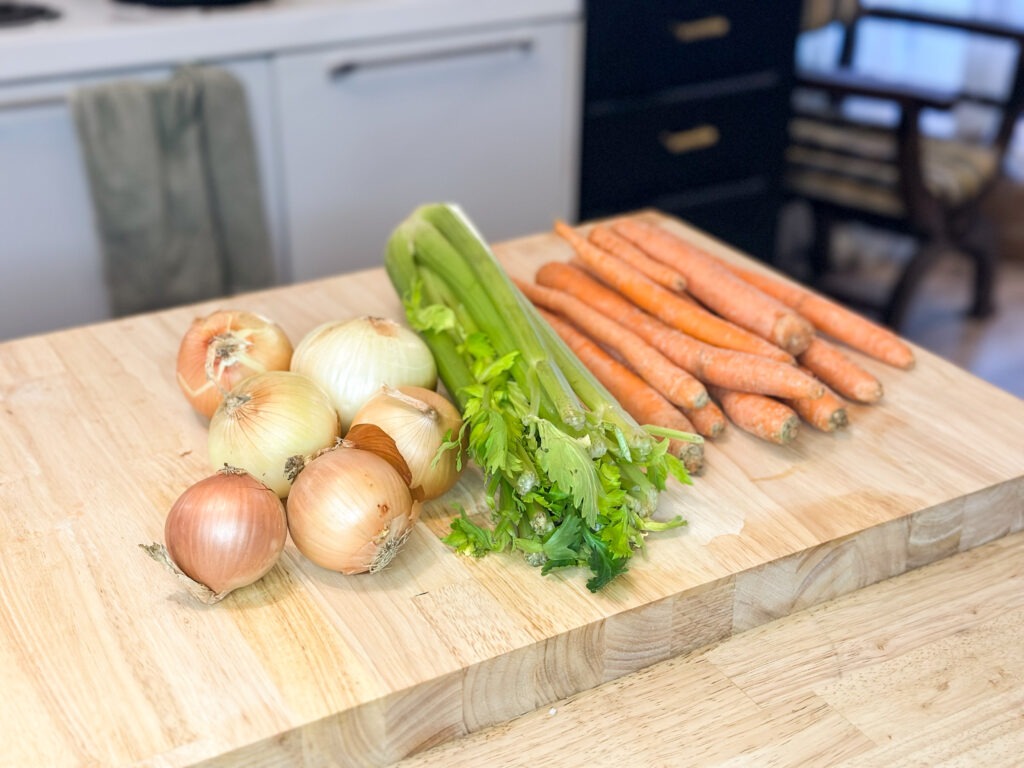 Onions, celery, and carrots on a cutting board. 