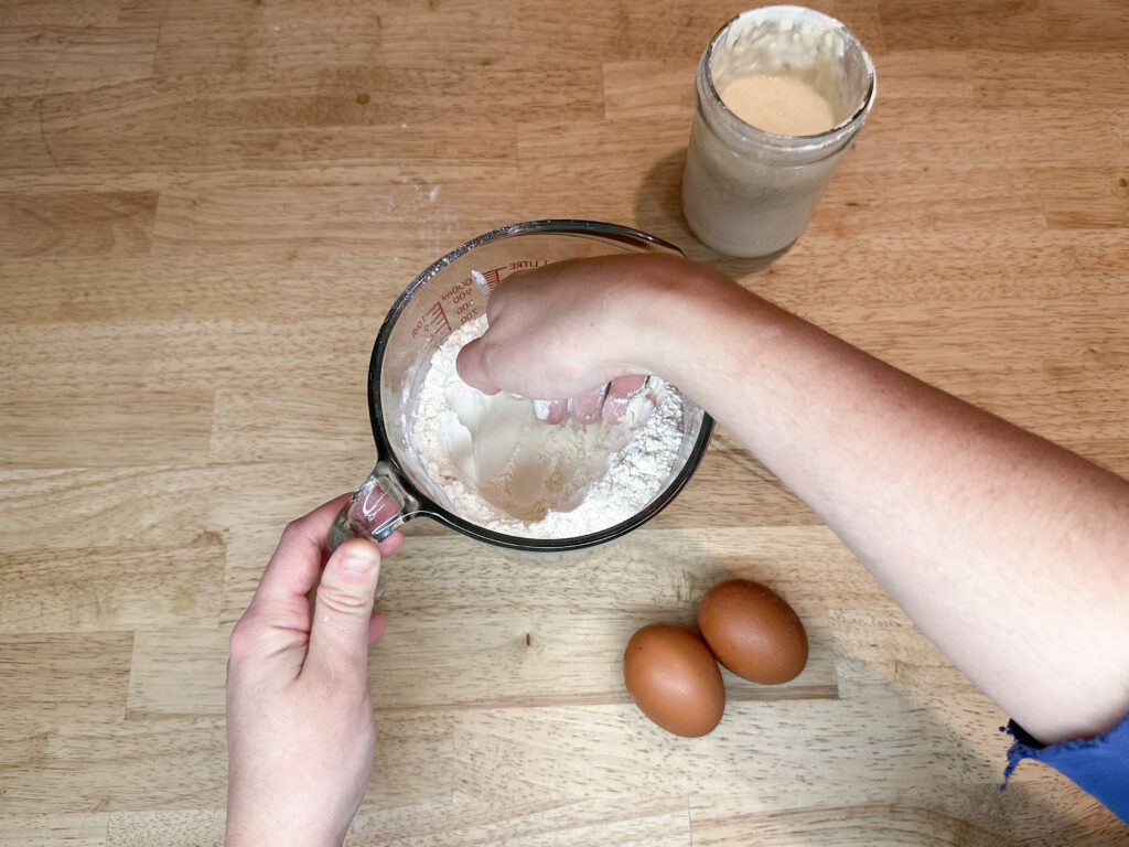 A woman's hands making a well in the middle of a flour mixture before adding the wet ingredients to the batter.